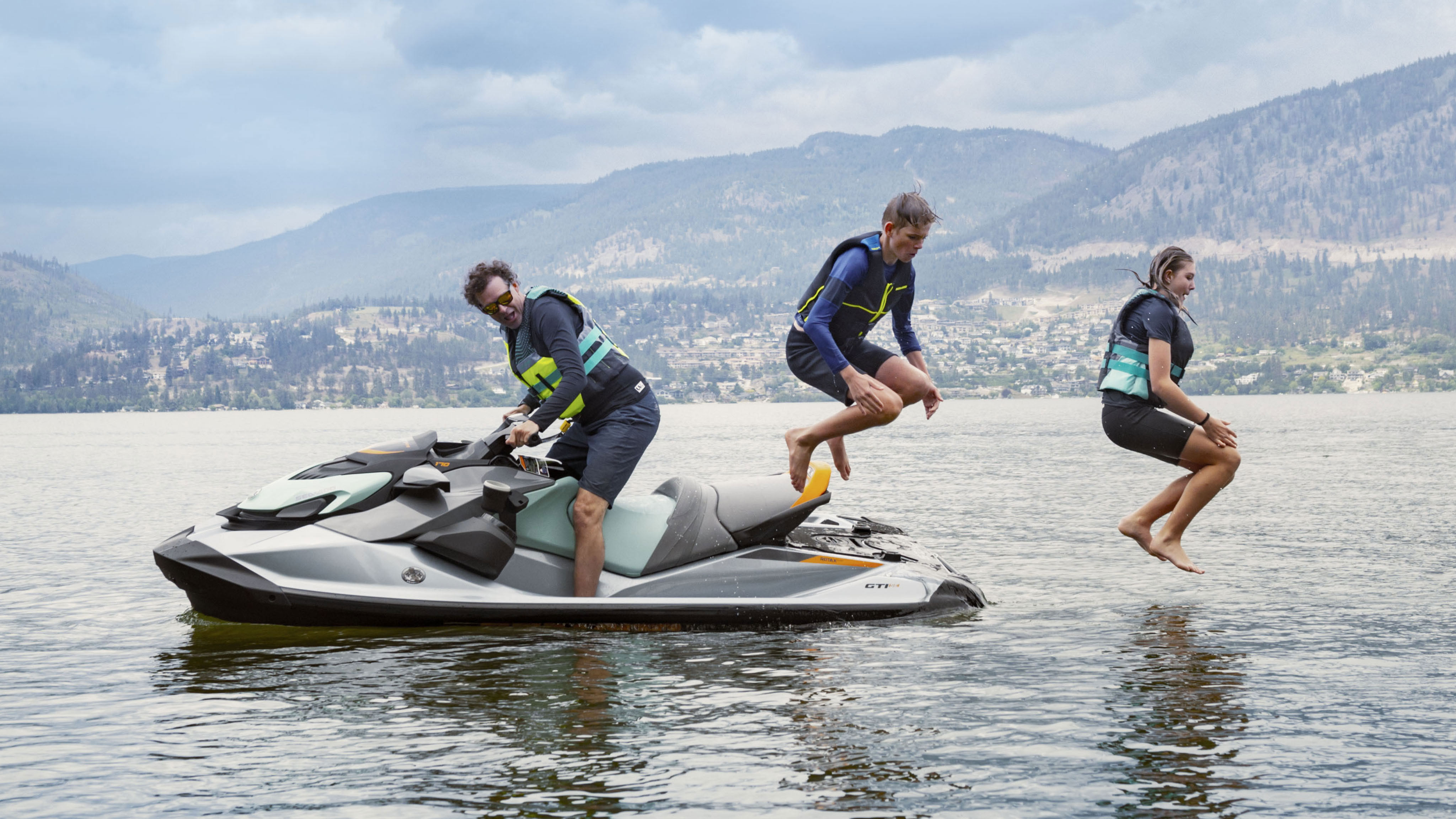 A dad on a Sea-Doo GTI while his two kids are jumping in the water